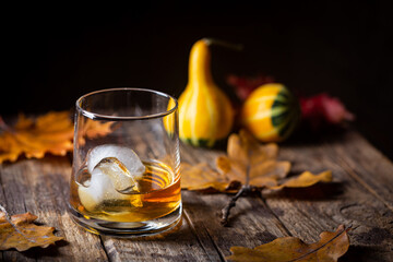 Glass of scotch whiskey and ice on wooden background with autumn leaves
