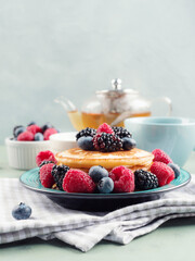 Stack of pancakes with fresh berries served in a dish with green tea.