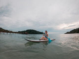 asian woman playing stand up paddle board in the sea when sunset.