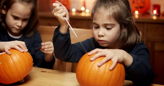 two cute little girls are cutting a pumpkin on the table for halloween