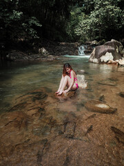 sexy asian woman in bikini in the stream water playing with wild fishes. transparent water in waterfall with many natural fish. Thailand travel concept.