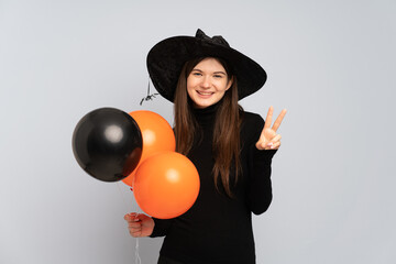 Young witch holding black and orange air balloons smiling and showing victory sign