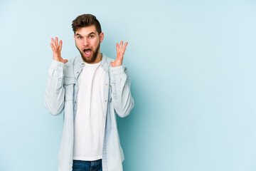 Young caucasian man isolated on blue background celebrating a victory or success, he is surprised and shocked.