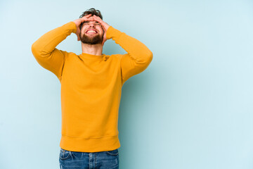 Naklejka premium Young caucasian man isolated on blue background laughs joyfully keeping hands on head. Happiness concept.