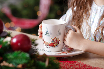 Little giirl hands keeping a cupof tea  standing on the table. Christmas and New Year. Winter holidays concept