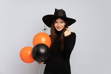 Young witch holding black and orange air balloons making money gesture