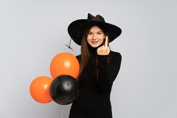 Young witch holding black and orange air balloons doing coming gesture