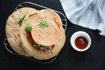 Metal cooling rack with doner kebabs served in pita bread, above view on a black stone background, horizontal shot