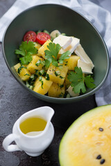 Salad with yellow watermelon cubes, herbed chopped cucumber and cheese slices served in a green bowl, vertical shot