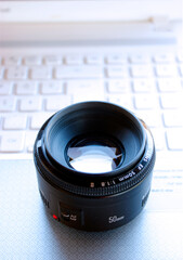 A DSLR camera objective is standing on a white computer keyboard surface