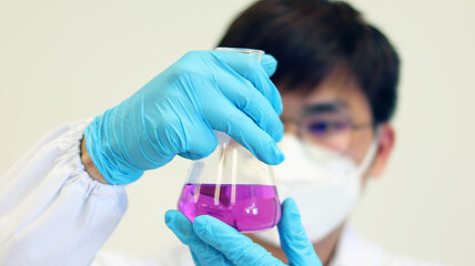 The scientist wear blue nitrile gloves holding Erlenmeyer Conical flask, with purple violet solvent forming reaction boric acid and ammonia solution analysis in wastewater sample. Selective focus.