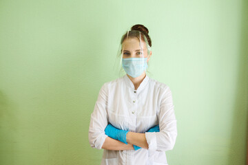 Doctor, medical specialist, beautician, dentist is wearing protective shield, mask and rubber gloves. Medical uniform. Green wall background. Indoors in clinic. 