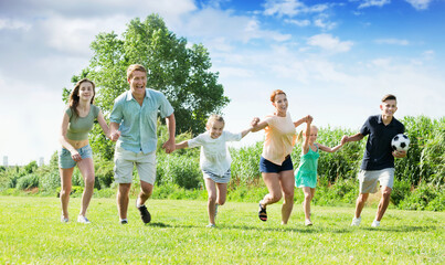 Positive glad mother and father with four happy kids having fun and running on green lawn in park