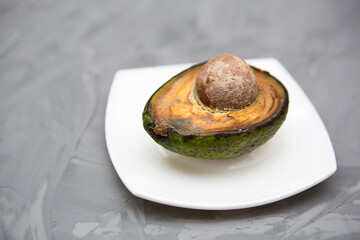 Spoiled avocado with green mold and black spots of rot and fungus on a gray background. Cut natural fruit, half with a round bone. Space for text