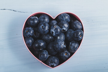 Blueberry heart.
Metallic heart-shaped mold filled with blueberries on a light blue wooden board.