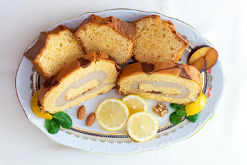 Bizcocho de limón y brazo gitano relleno de crema de café y vainilla con rodajas de limón servido en bandeja de lujo con decoración de frutos secos y hojas verdes.