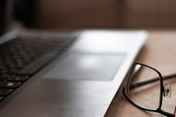 Background image of business office with laptop on wooden desk, focus on black hard rim glasses in foreground, copy space. Out of focus. Blurred