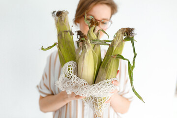 Young pretty girl on a gray background holding corn cobs in her hands