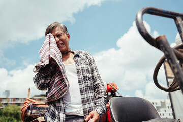 Asian senior farmer resting on a tractor after working at local farm.