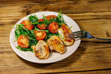 Fried chicken breast with salad of fresh arugula and cherry tomatoes on wooden table