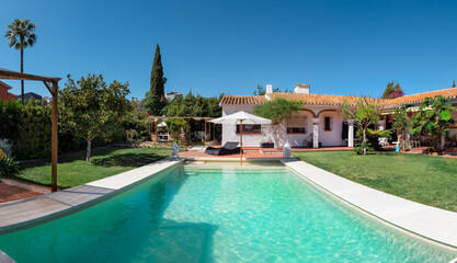 Exterior panorama of a relaxing holiday villa with a swimming pool with tanning ledge,chair...