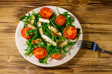 Tasty salad of fried chicken breast, fresh arugula and cherry tomatoes on wooden table. Top view