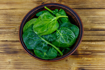 Fresh green spinach leaves in bowl on a wooden table. Top view