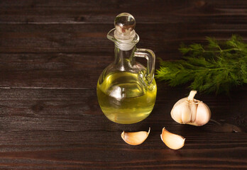 Garlic oil in a glass carafe on a wooden table, garlic next to it.