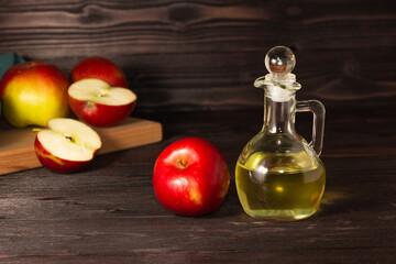 Apple cider vinegar in a glass decanter on a dark wooden table. Apples nearby.