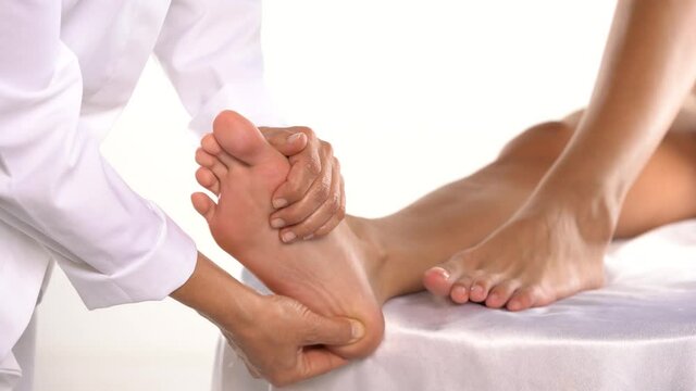 masseuse massaging the feet of a young woman on a white background