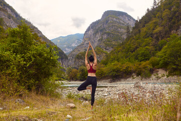 Naklejka na ściany i meble Yoga classes in nature. A woman does yoga in the mountains, near a mountain river flows. The concept of playing sports alone. Social exclusion