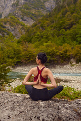 Fototapeta na wymiar Yoga classes in nature. The concept of playing sports alone. Social exclusion. A woman does yoga on rocks, near a mountain river flows