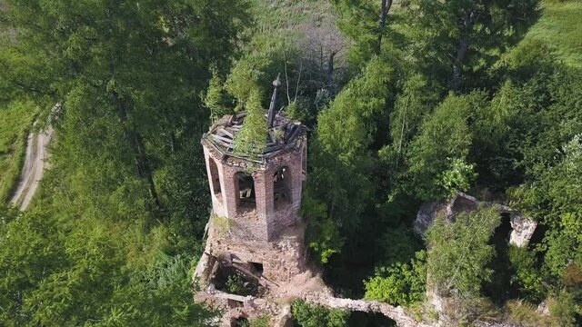 Aerial view of lush forest on a sunny summer day and an old church. Clip. Flying over ruins of the ancient stony church located among green trees.