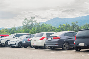 Fototapeta na wymiar Car parked in large asphalt parking lot with trees, cloudy sky and mountain background. Outdoor parking lot with fresh ozone and green environment of travel transportation concept