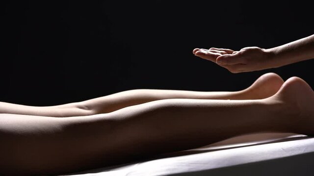 a massage of a young woman's legs in a salon on a black background