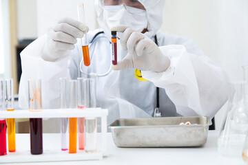 hands laboratory scientist PPE suite uniform wearing face mask protective with a tube of blood sample in lab. Diagnose checking coronavirus or covid-19 testing result