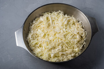 The cabbage is chopped and cooked for pickling in a bowl on a gray background.