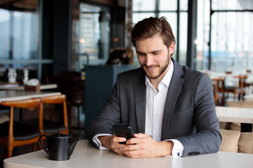 Businessman using smartphone in cafe, smiling and relaxing