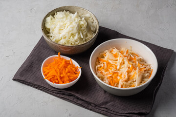 Cabbage and carrots are chopped and prepared for pickling in three bowls on a gray background. The best natural probiotic. Fermented product