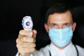 Coronavirus symptoms, man in medical mask measures body temperature. Doctor with digital isometric non-contact thermometer in his hand, safety measures during covid-19 quarantine