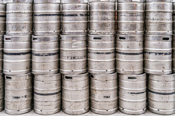 Wall of used and scratched stainless steel beer barrels or kegs. Stacked in a row large silver or metallic colour alcohol barrels or containers