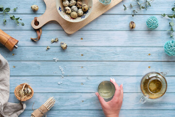 Quail Easter eggs and natural Spring decorations, twigs and eucalyptus. Hand holding glass with tea