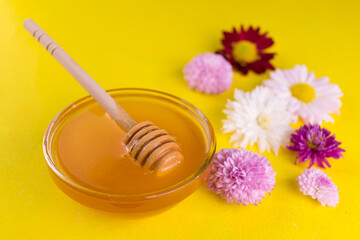 
Honey in a bowl and flowers on a bright yellow background. Close-up.