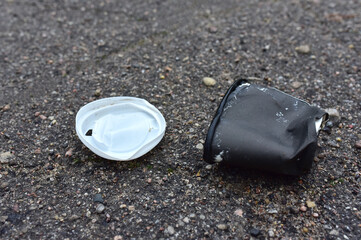 Crumpled a paper coffee cup on asphalt. Discarded disposable coffee cup with a plastic lid on road. Out of shape crushed paper cup. Abandoned garbage of disposable cups.
