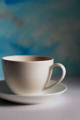 White cup of tea and saucer on blue background.Blue coffee cup on the white table over blue grunge background