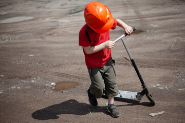 A child on a scooter on the street. A boy in an orange helmet rides a scooter. 