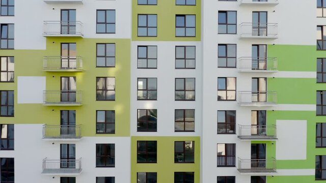 Slow panning shot rising up the colorful green and white facade of a high-rise building in an urban complex passing rows of windows to the rooftop