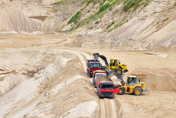 Obraz na płótnie Canvas Wheel loader loading sand into heavy dump truck at the opencast mining quarry. Dump truck transports sand in open pit mine. Quarry in which sand and gravel is excavated from the ground.