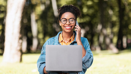 Black Woman Talking On Cellphone Working On Laptop Sitting Outdoors