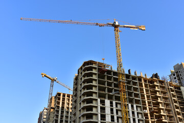 Tower cranes working at construction site on blue sky background. Construction process of the new modern residential buildings